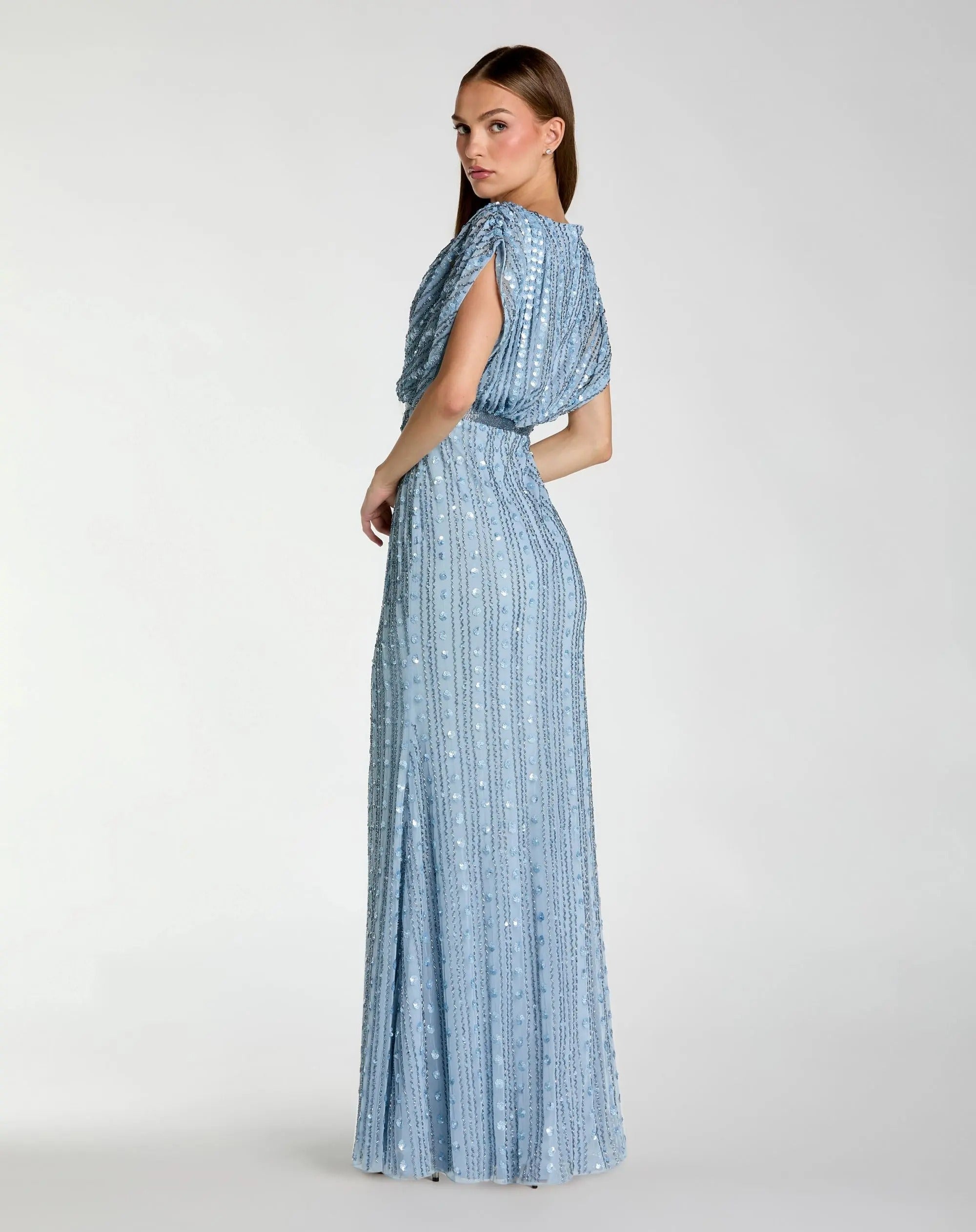 A woman stands sideways against a plain white background wearing the Mac Duggal 23081 Long Formal Dress—a sleeveless, floor-length gown in light blue with sequin embellishments and vertical stripes.